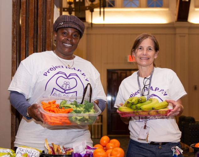 Drs. Jones and Stevenson at the snack table holding healthy fruits and vegetables