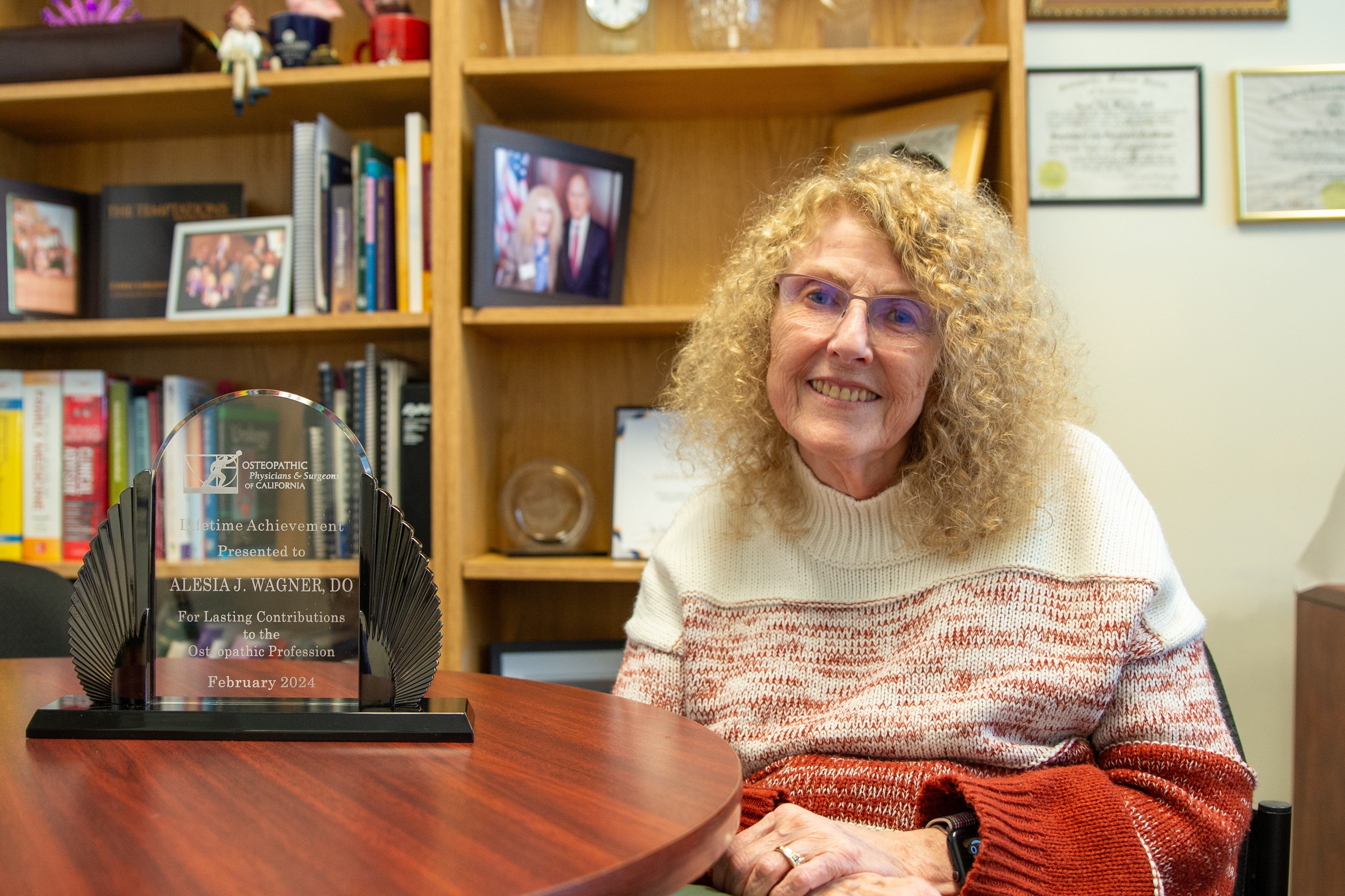 Dr. Alesia Wagner sits at a wooden table next to her lifetime achievement award