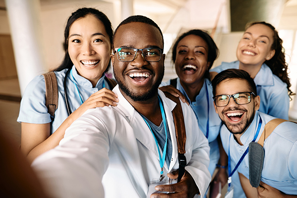An image shows a group of five medical students smiling and laughing as they pose for a group selfie. Medical students are the prime beneficiaries of working with preceptors, but the preceptors derive benefits as well. (iStock / Drazen Zigic)