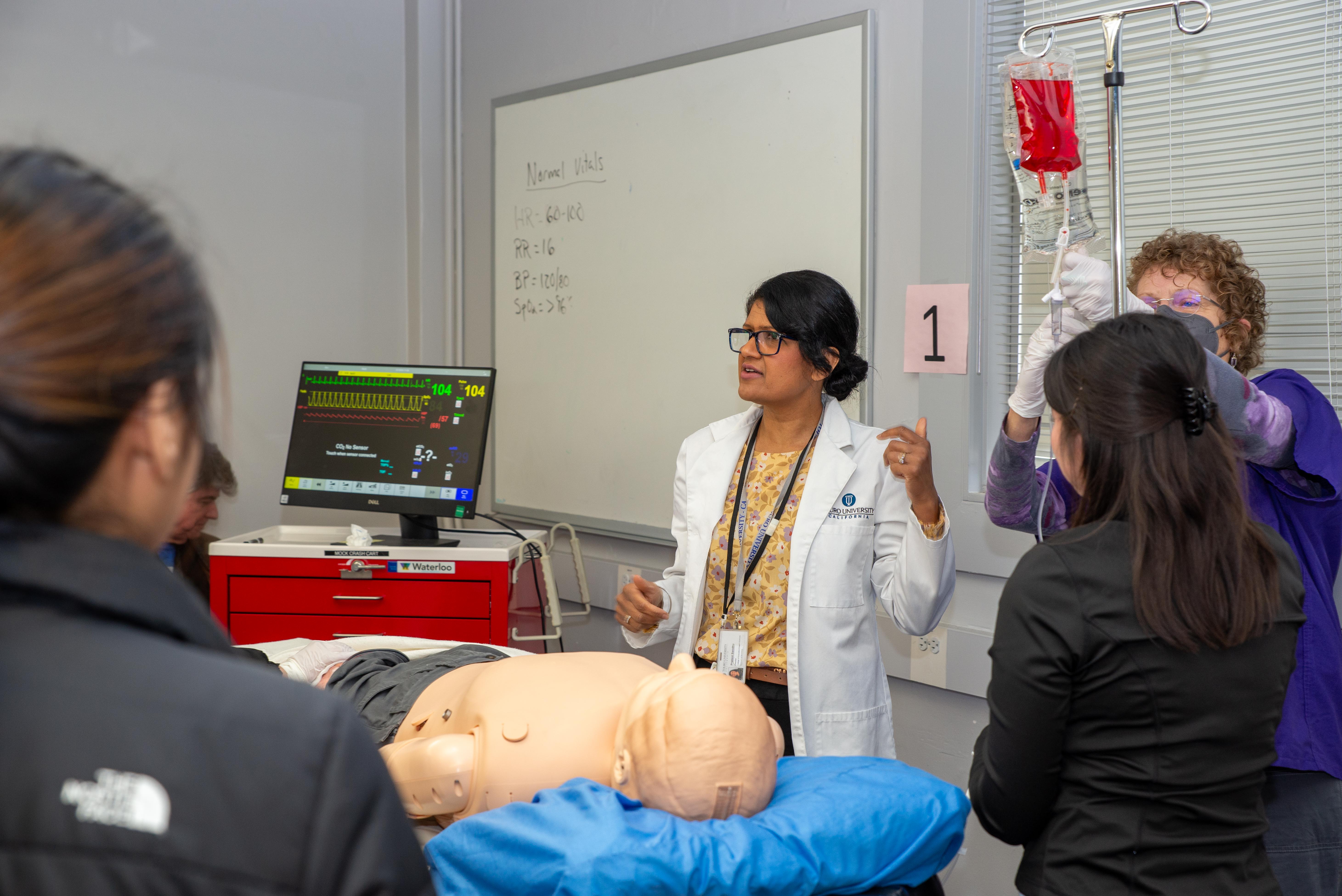 Dr. Prabjot Sandhu, Assistant Dean of the Director School of Nursing demonstrates vitals and medical procedures to students with a simulator mannequin 