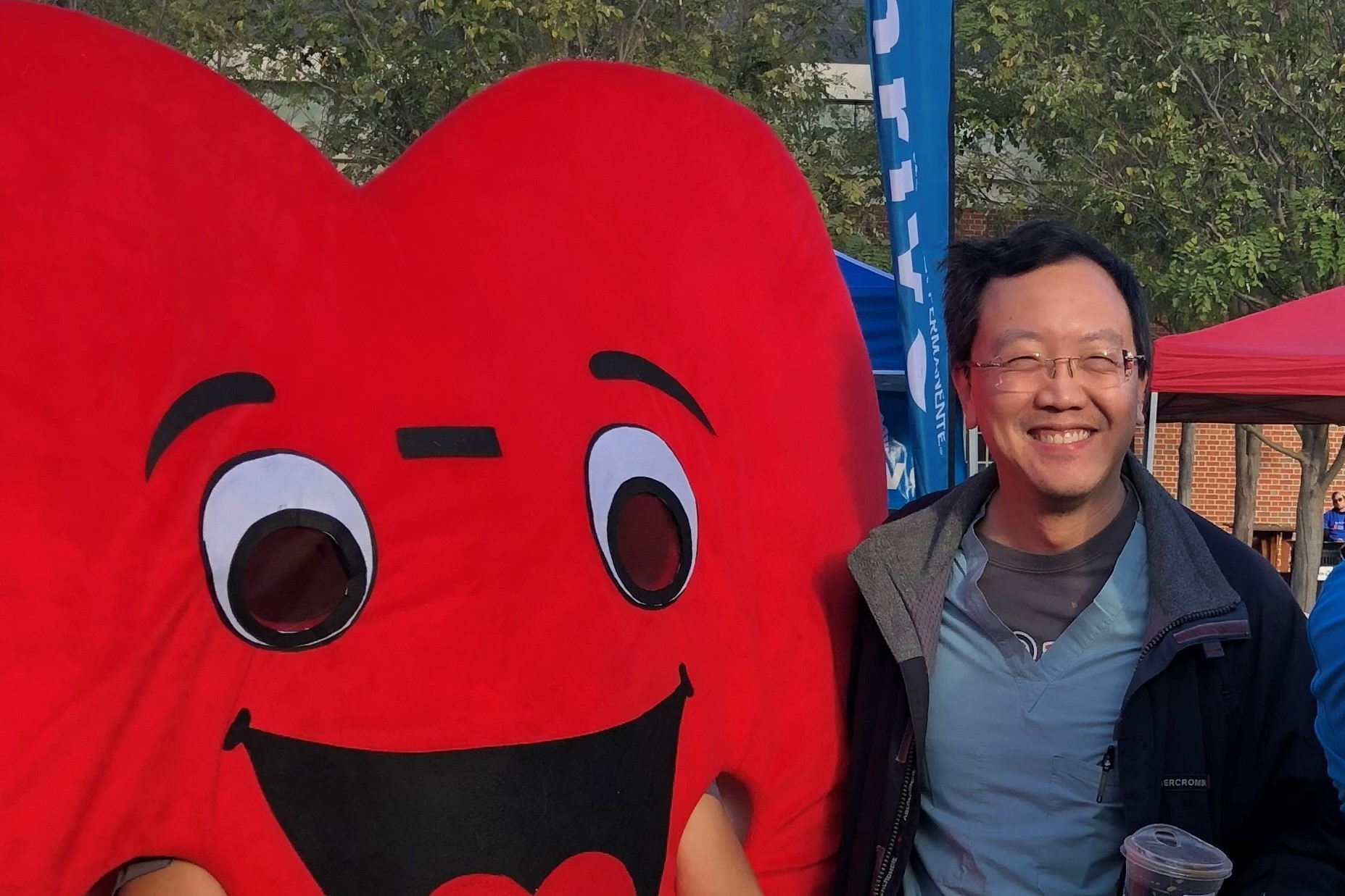 Dr. John Yeung stands next to a person-sized, smiling, red heart mascot.