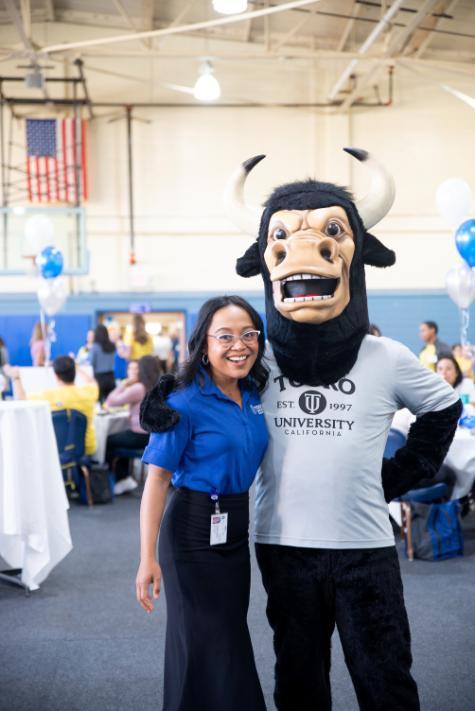 Fraylanie Aglipay and the Touro bull mascot standing in the gym with tables and students behind them