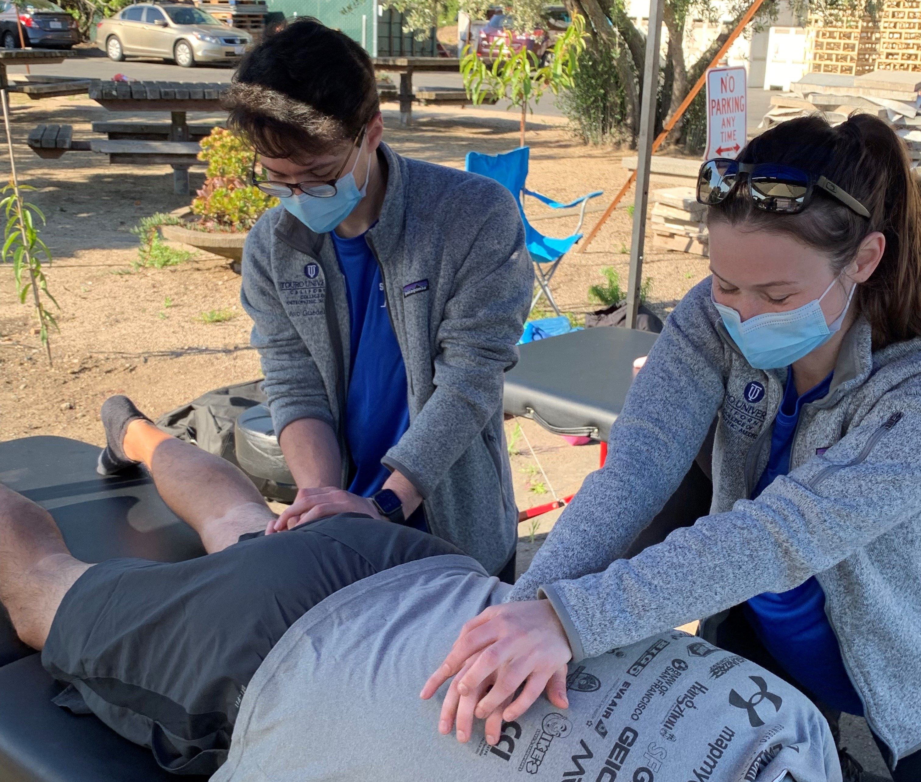 Student doctors demonstrate OMM treatments to an athlete on a treatment table at a running event