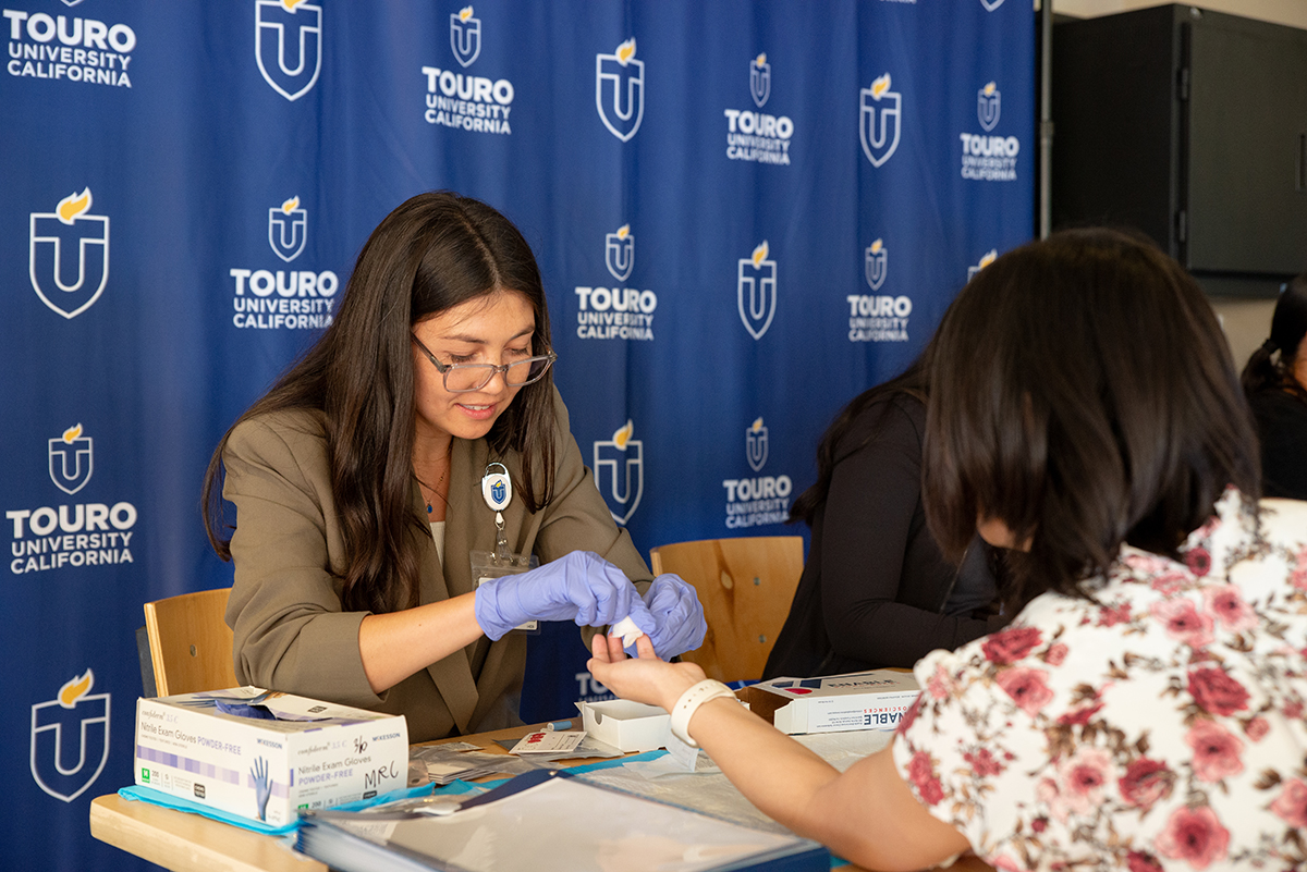 A photo shows a Touro University California Student Doctor administering diabetes screening.