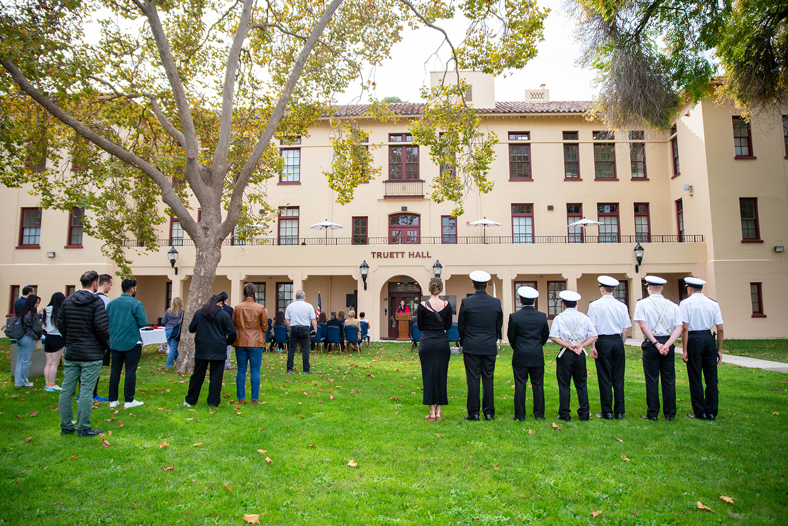 A photo shows members of the TUC Community as they assemble on the green lawn of Truett Hall for the 2025 Veterans Day Celebration.