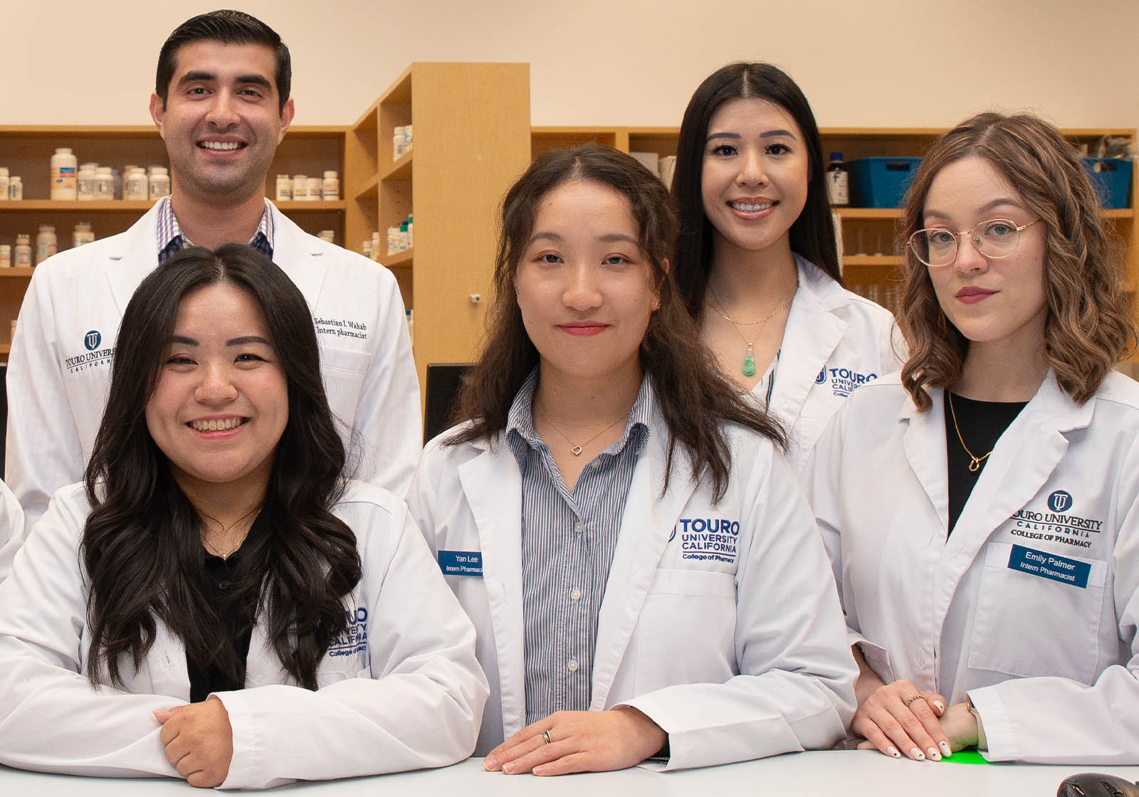 A group of Pharmacy students stand behind a counter and smile for a group photo