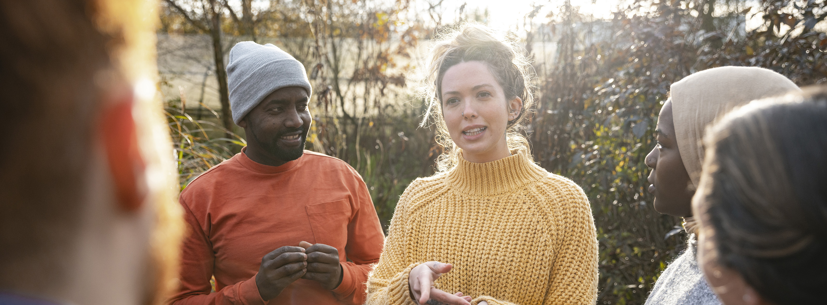 A multiracial group of volunteers wearing warm casual clothing and accessories on a sunny cold winters day. They are talking before they start working on a community farm, planting trees and performing other tasks.