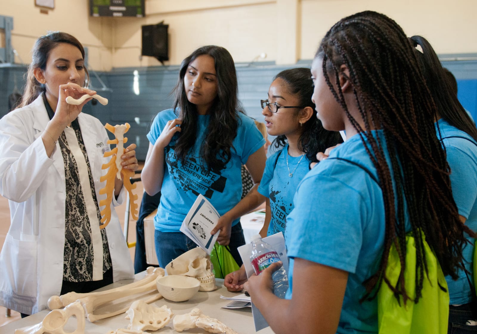 woman in white coat doing a demonstration with a skeleton for a group of teens