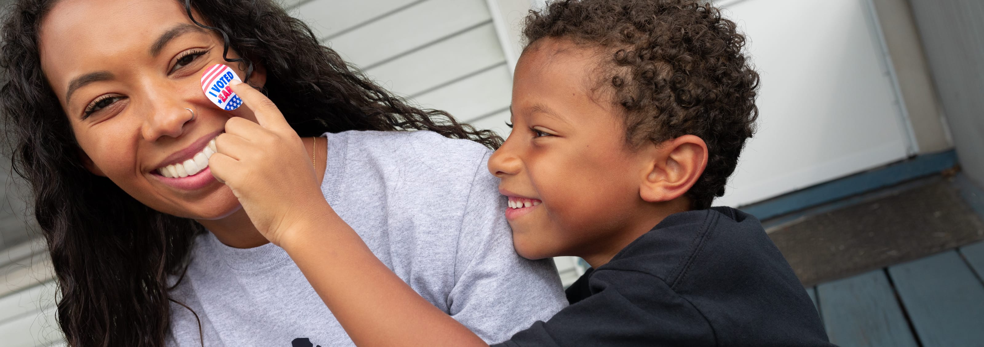 Black mother wearing BLM t-shirt with child holding up an I voted sticker