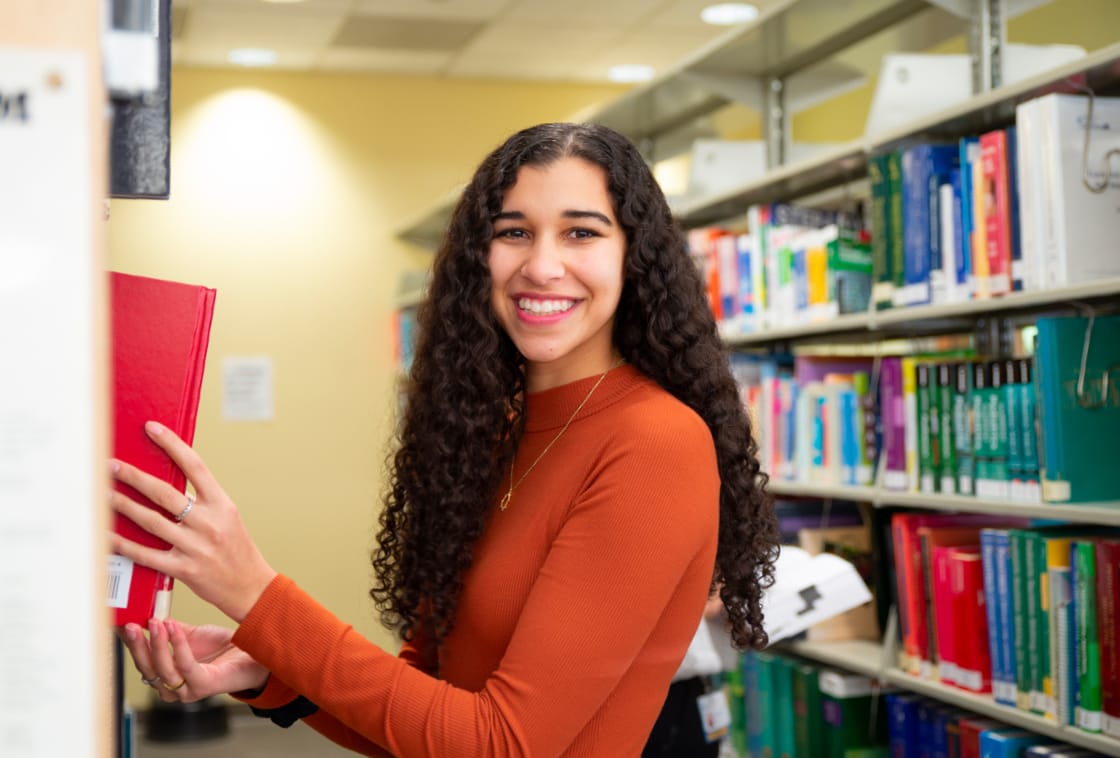 smiling student pulling library book off the shelf