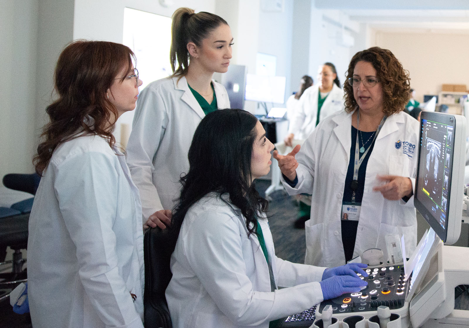 Three Touro California Sonography students intently listen to their teacher while she reviews a sonograph on a monitor.
