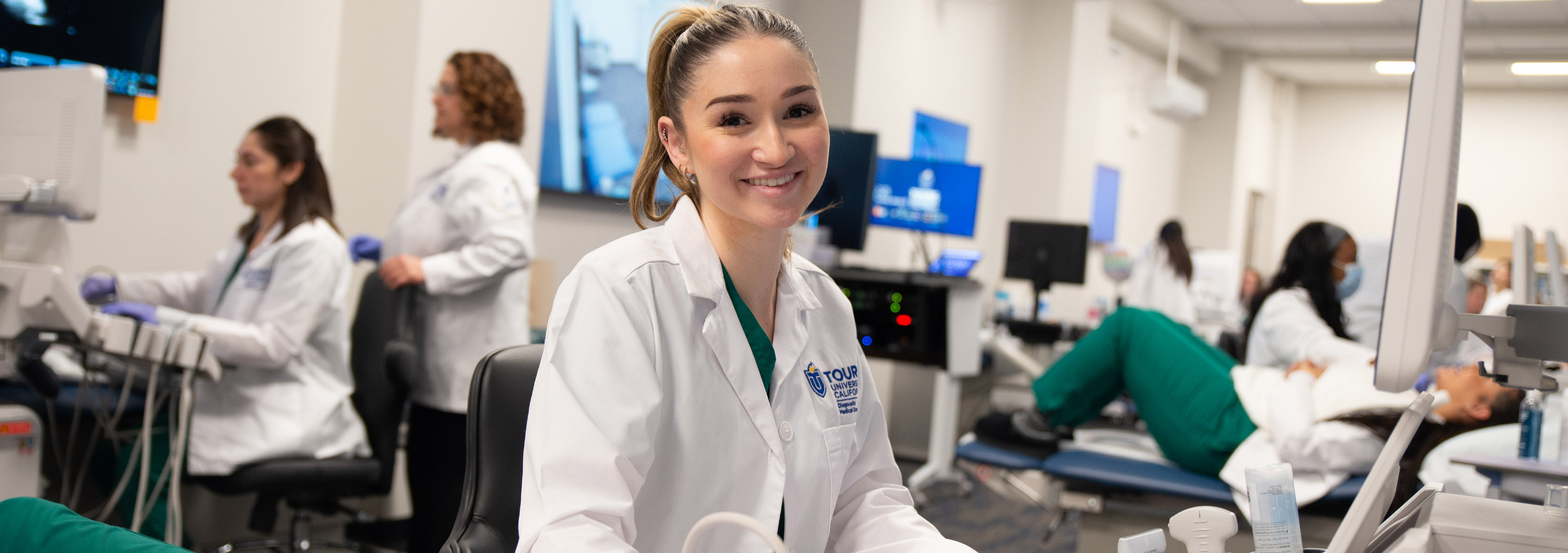 A Touro California Sonography student smiles for the camera while giving another student a sonogram.