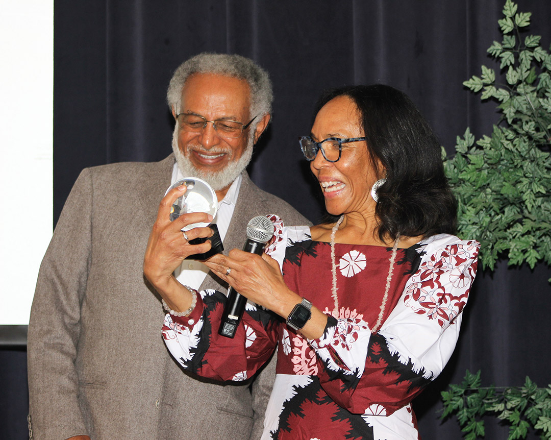 The photo shows Dr. Assefaw Tekeste Ghebrekidan and Dr. Gayle Cummings smiling as they look at the Hero Award presented to Dr. Ghebrekidan.