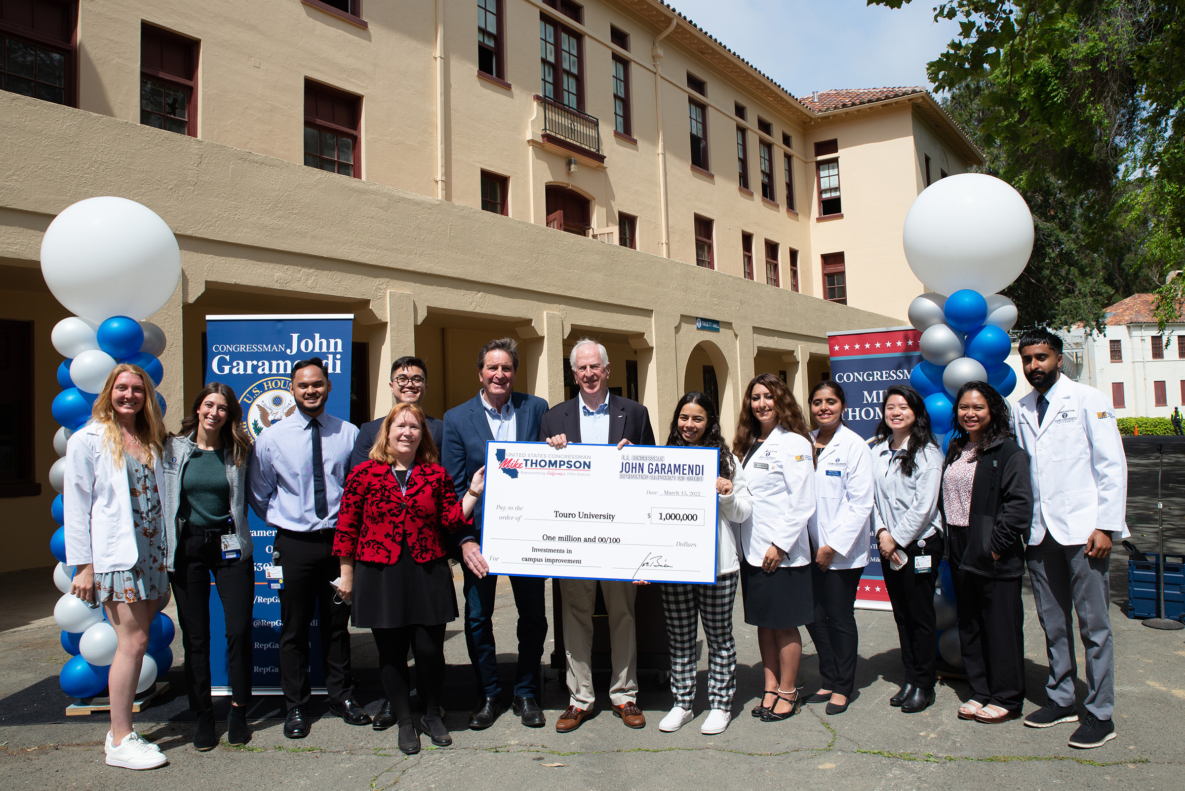 Group with students, Provost, and Congressmen stand in front of Truett Hall holding large check