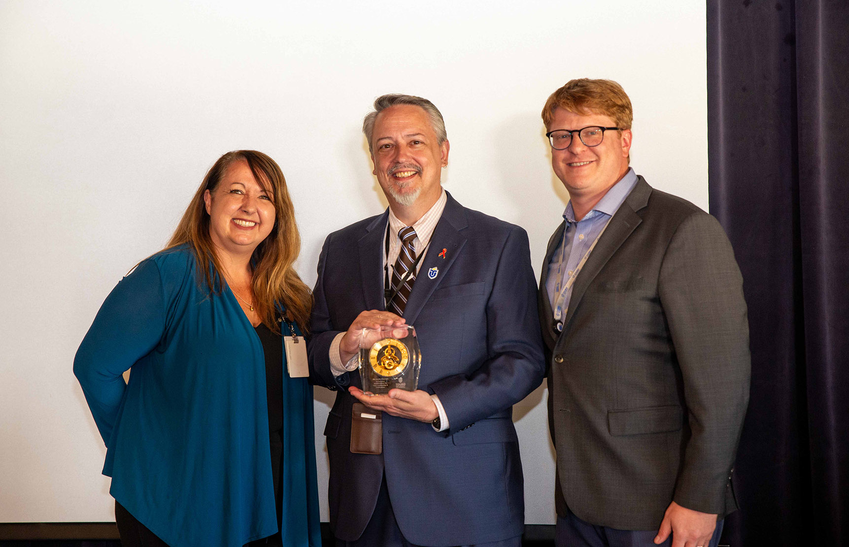 A photo shows Touro University California College of Pharmacy Dean Dr. Jim Scott, center, as he holds an award while flanked by College of Osteopathic Medicine Dean and Interim Chief Academic Officer Dr. Tami Hendriksz, left, and Vice President and Interim CEO Newman Hoffman, right, during an event to celebrate Scott\'s tenure at TUC, Monday, Aug. 19, 2024.