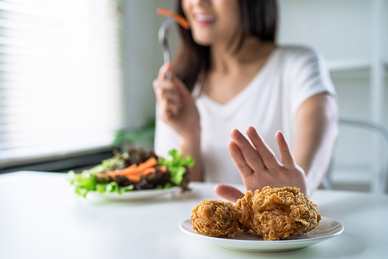 An image from Panupong Piewkleng / iStock shows a woman opting to eat a salad while turning aside a plate of fried chicken. If the holidays pulled you away from your healthy diet and exercise routine, now\'s a great time to get back on track for 2024.