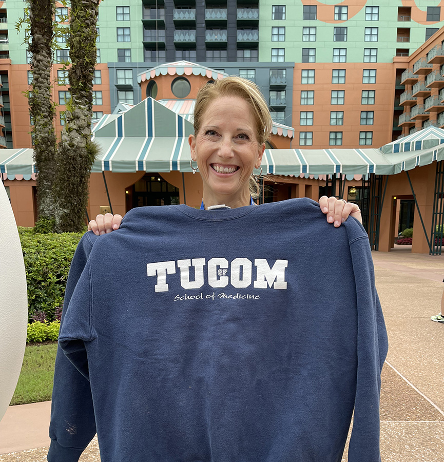 A photo shows Dr. Jennifer Himmel, Touro University California Class of 2002, as she shows off a sweatshirt from the College of Osteopathic Medicine when it was located in San Francisco. Himmel is shown outside the Walt Disney World Swan Resort during the American Osteopathic Association\'s annual Osteopathic Medical Education Conference in Orlando, Florida, Saturday, Oct. 7, 2023.