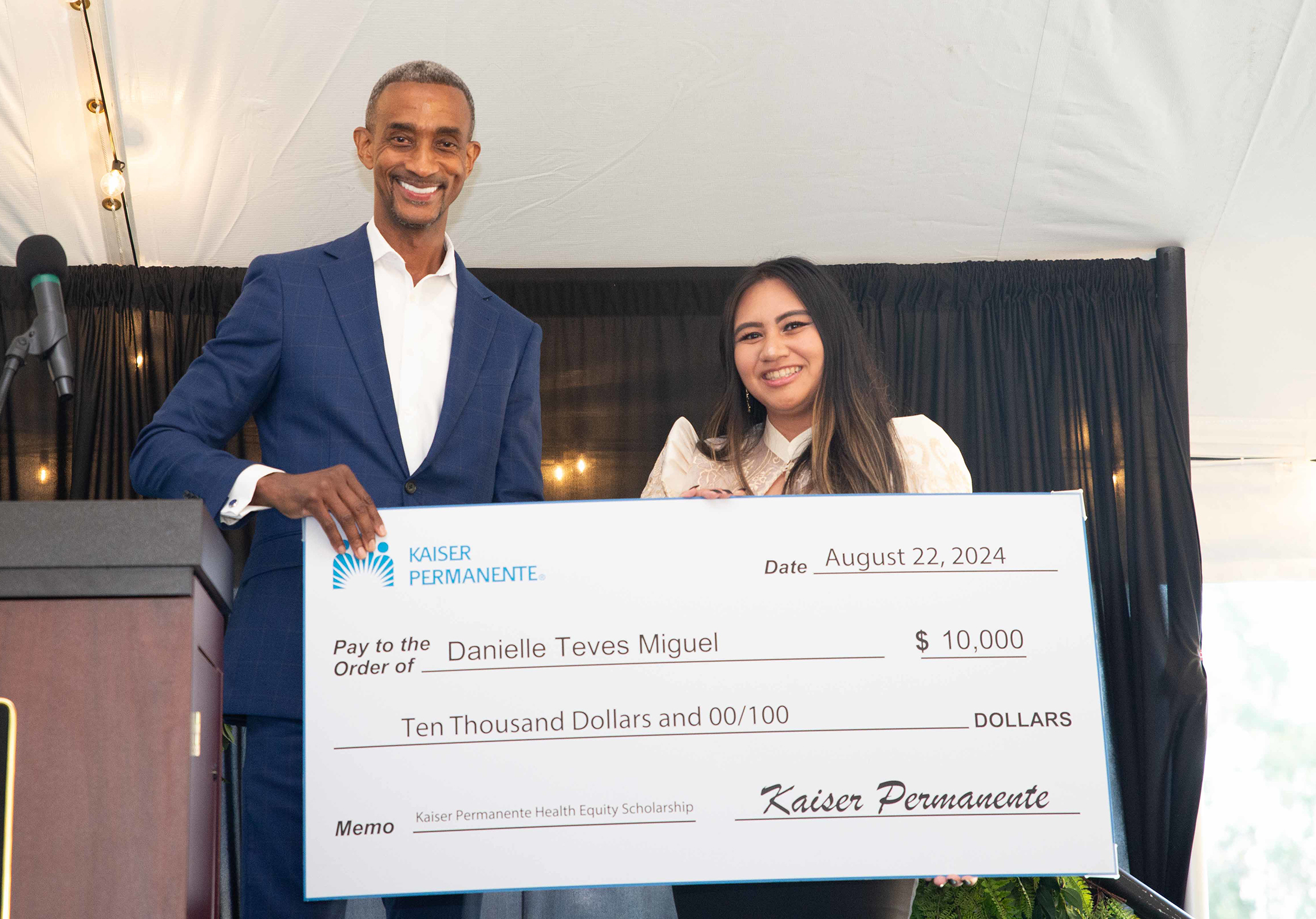 Darryl Curry holding up a check and presenting it to a TUC Student on the stage the 2024 Mosaic Gala.