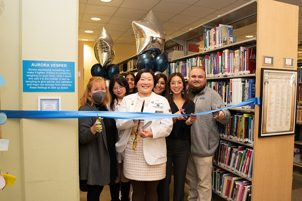 Students and faculty cut a ribbon with scissors inside the campus library.