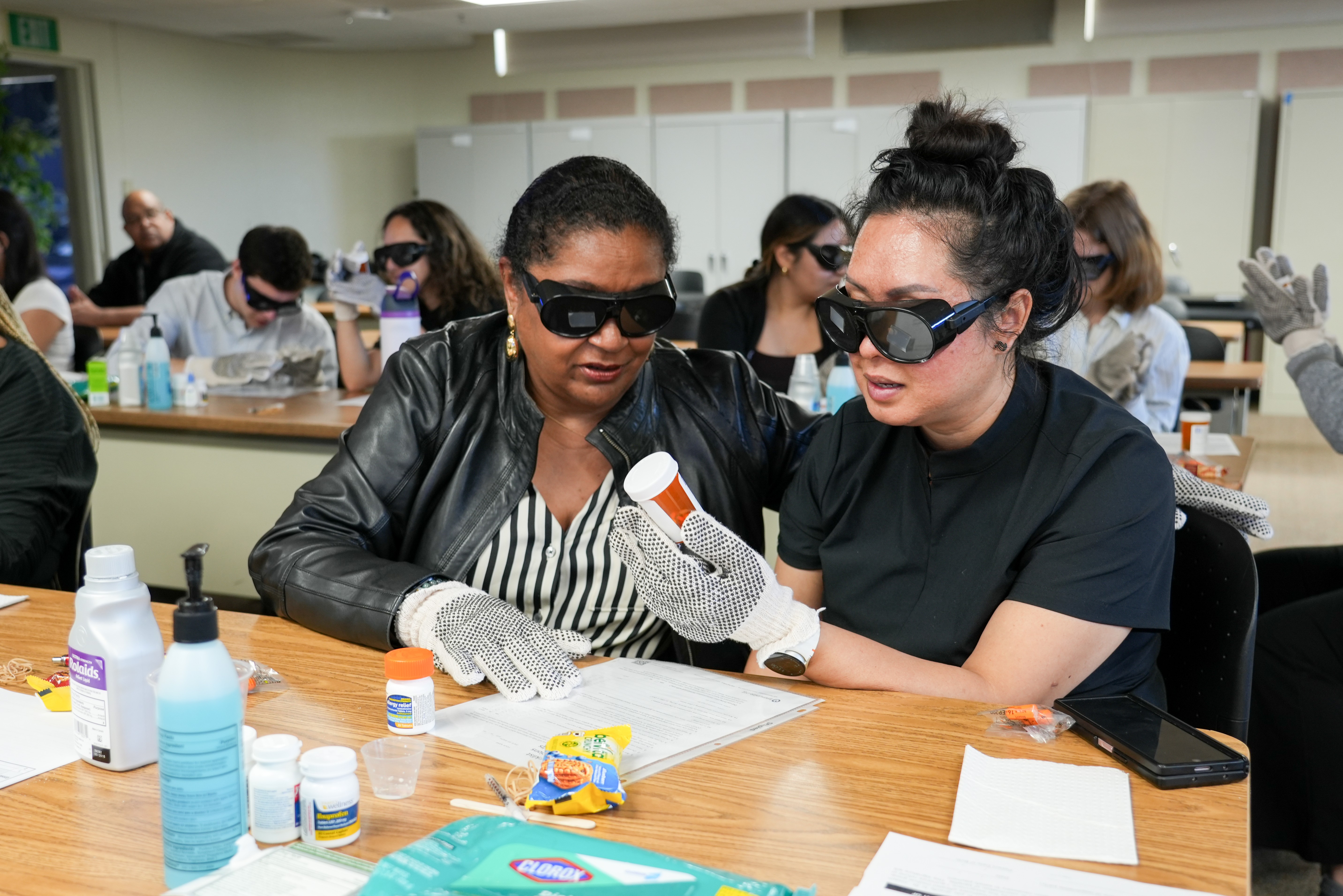 Two students sit together and perform hands-on tasks that enable them to experience hearing, vision, and mobility disabilities.