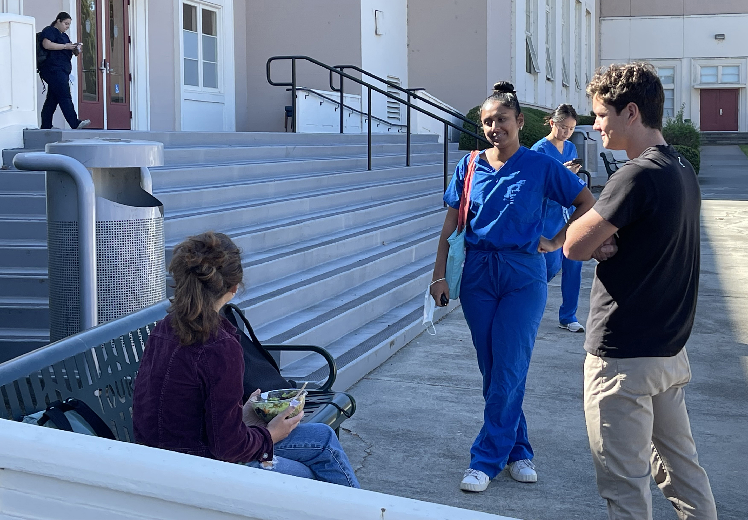 A photo shows three Touro University California students, one with a protective face mask handy at her wrist, maintaining some social distance as they chat outside Lander Hall, Tuesday, Oct. 15, 2024. The winter virus season begins Nov. 1, 2024.