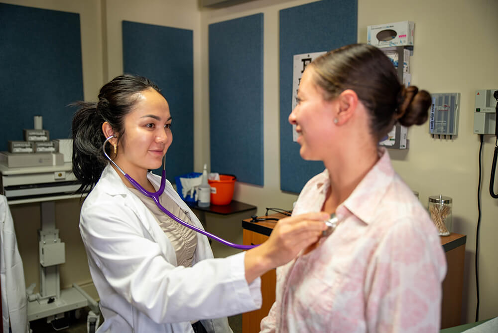 Female doctor in white coat examining female patient with a stethoscope